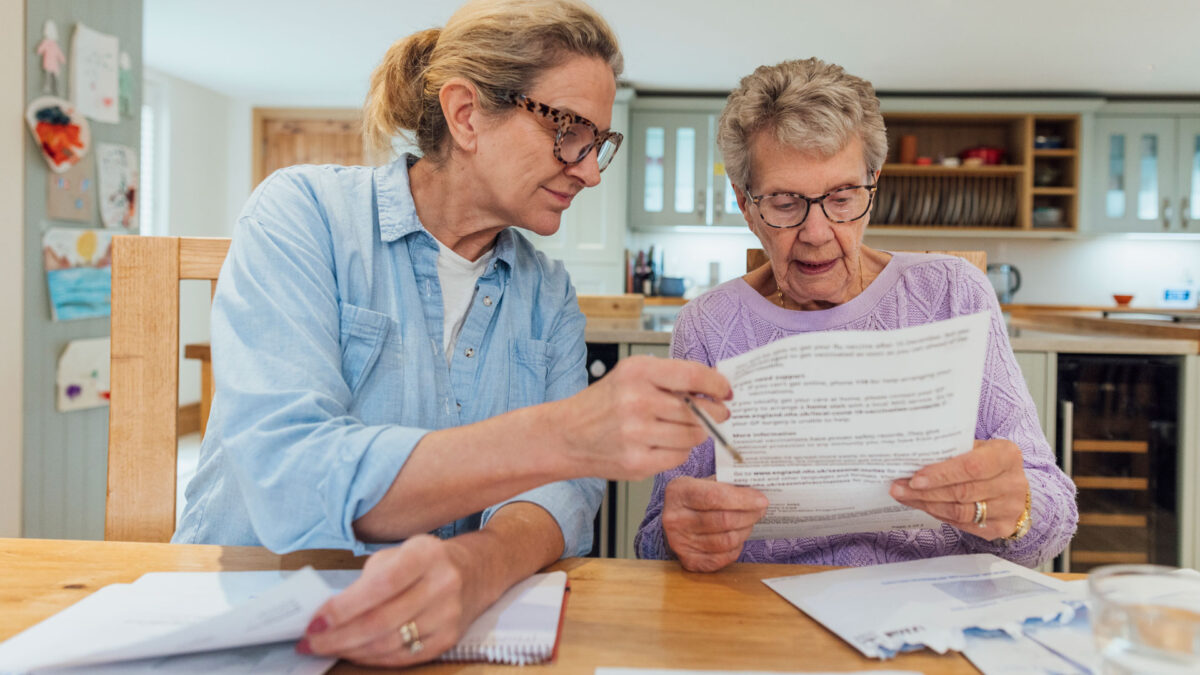 Daughter helping mom look over paperwork at kitchen table