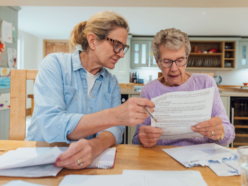 Daughter helping mom look over paperwork at kitchen table