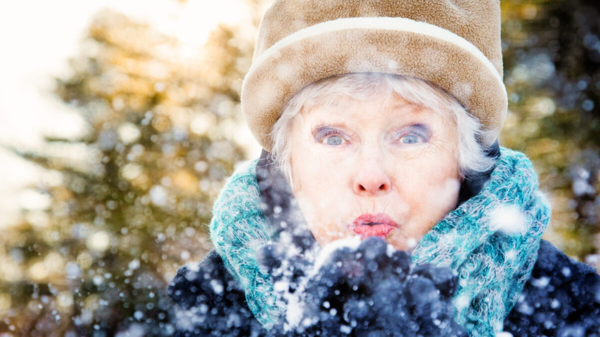 Close-up of a senior woman blowing snow to camera