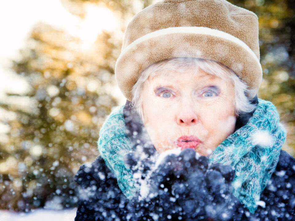 Close-up of a senior woman blowing snow to camera