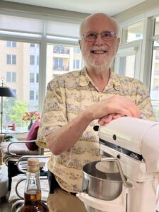 Jay, the community baker, smiling beside his stand mixer in the kitchen.