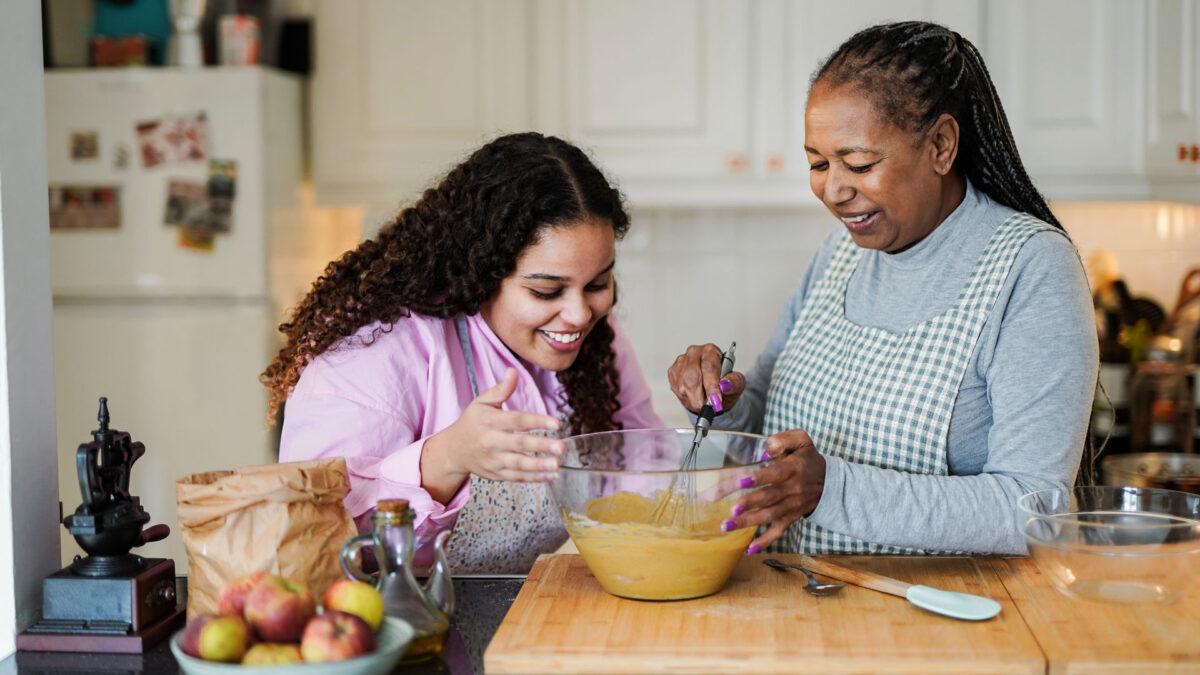 Happy african grandmother and grand daughter preparing fresh cake in the morning inside house kitchen.