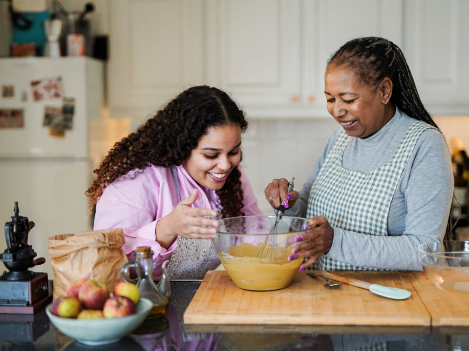 Happy african grandmother and grand daughter preparing fresh cake in the morning inside house kitchen.