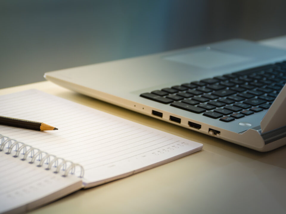 Office workplace with laptop and blank note book paper with pencil under warm light of desk lamp.