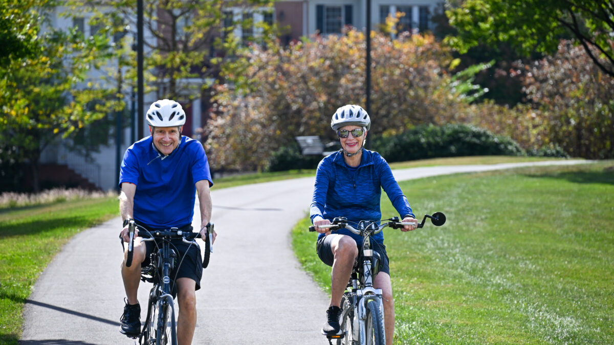 Senior couple biking together in park on sunny day